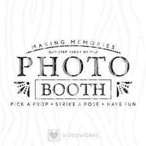 May include: Black and white sign with the text "Making Memories" and "Step Right Up" above the words "Photo Booth". Below the words "Photo Booth" is the text "Pick a Prop. Strike a Pose. Have Fun". The sign also includes the text "Woodworks" and a small heart with the letter "W" inside.