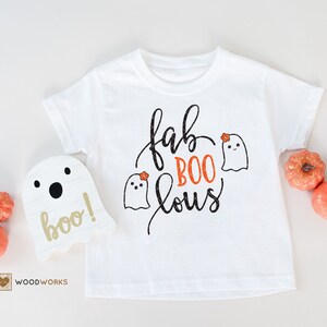 Op de afbeelding: Wit T-shirt met zwarte tekst die "fab BOO lous" zegt en een klein oranje bloemetje op elk van de drie geesten.