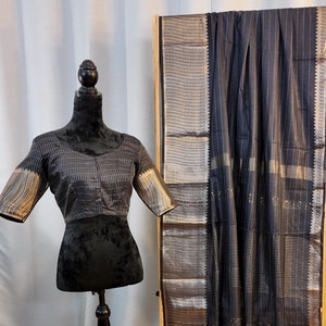 May include: A black and silver striped saree with a gold border. The saree is draped over a wooden stand and a black blouse is displayed on a mannequin.