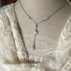May include: A silver-toned necklace with a cameo pendant and a dangling pearl. The necklace features small pearls and a delicate chain. The cameo pendant has a blue and white design. The necklace is displayed on a mannequin.
