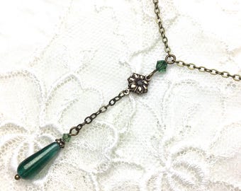 May include: An antique bronze-toned necklace with a dark green teardrop-shaped pendant. The necklace features a floral accent and small green crystal beads. The chain is delicate and the pendant is approximately 1 inch long.