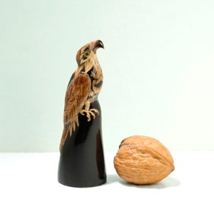 May include: A carved wooden eagle figurine with brown and black markings, standing on a black base. A brown walnut is in the foreground.