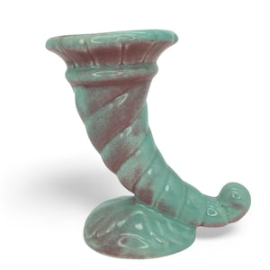 Puede incluir: Un jarrón de cerámica con forma de cornucopia en una combinación de colores turquesa y granate. El jarrón tiene un diseño en espiral en el cuerno y una parte superior acampanada. La base tiene forma redondeada. Es un objeto decorativo.
