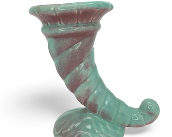 Puede incluir: Un jarrón de cerámica con forma de cornucopia en una combinación de colores turquesa y granate. El jarrón tiene un diseño en espiral en el cuerno y una parte superior acampanada. La base tiene forma redondeada. Es un objeto decorativo.