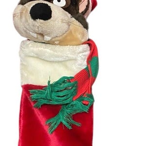 Könnte beinhalten: Ein Plüsch-Weihnachtsstrumpf mit dem Kopf einer Zeichentrickfigur, die einen roten Weihnachtsmannhut trägt. Der Strumpf ist rot mit einer weißen Manschette und einem rot-grünen Schal. Eine Schlaufe zum Aufhängen ist angebracht.