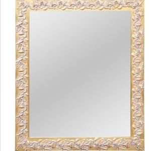 May include: A rectangular mirror with a gold-colored frame. The frame features a detailed, raised floral design in a cream color. The mirror's reflective surface fills the center of the frame, creating a classic decorative piece.