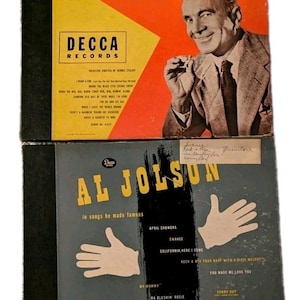 May include: Two vintage Al Jolson record albums. The top album cover is yellow and orange with a portrait of Al Jolson. The bottom album cover is gray with white hand illustrations and song titles. Both albums are from Decca Records.