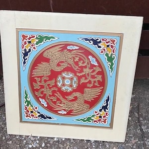 May include: A white framed square panel with a red, gold, and blue painted design featuring two stylized phoenixes in a circle. The phoenixes are facing each other with their wings spread. The background is a light blue with white clouds and gold accents.
