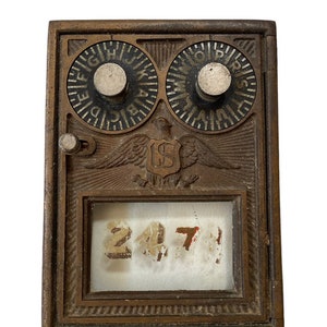 May include: Vintage bronze-coloured mailbox door with two circular dials featuring letters, an eagle emblem, and a small window displaying the numbers 2471. The door has a rectangular shape and a vintage aesthetic.