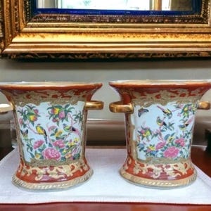 May include: Two matching decorative vases with a red and gold rim and base. The vases feature a white center with colorful birds, flowers, and butterflies. Each vase has gold handles.