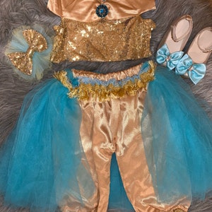 May include: A gold and blue costume for a child, featuring a sequined top, pants with gold trim, a blue tulle skirt, and a gold bow. The costume is complete with a pair of gold shoes with blue bows.