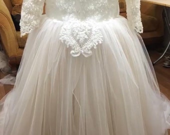 Puede incluir: Un vestido de tul blanco con mangas largas y detalles de encaje. El vestido tiene un corpiño ajustado y una falda completa.