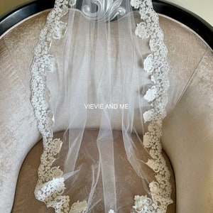 May include: A white bridal veil with a delicate lace trim. The lace features a floral design with a scalloped edge.