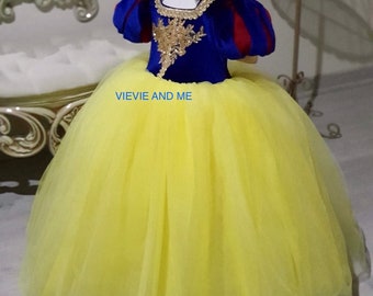 May include: A yellow tulle dress with a blue velvet bodice and red and white accents. The bodice has gold embroidery and a white collar. The dress is for a child and has a bow on the head.