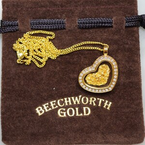 May include: A gold heart-shaped pendant with a clear glass insert filled with gold flakes. The pendant is on a gold chain and is in a brown velvet pouch with the text "Beechworth Gold".