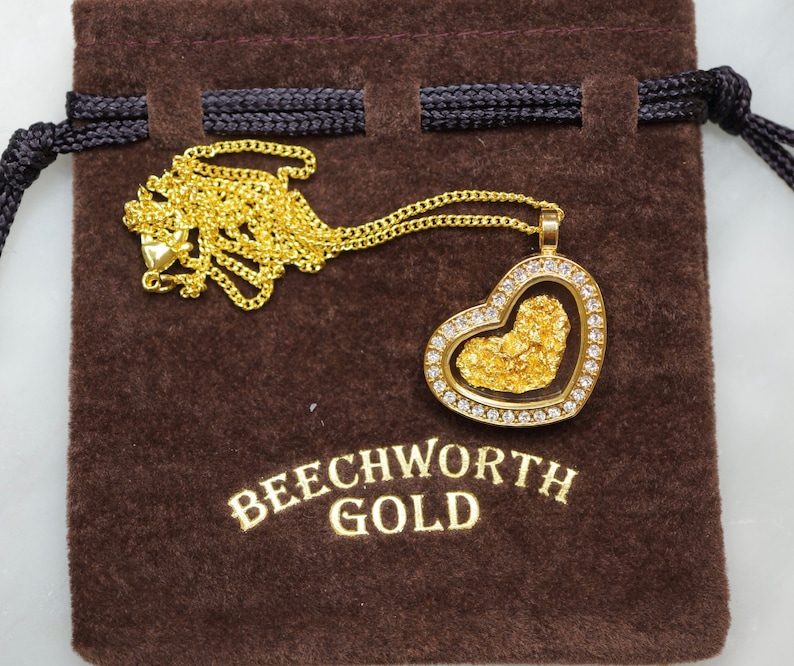 May include: A gold heart-shaped pendant with a clear glass insert filled with gold flakes. The pendant is on a gold chain and is in a brown velvet pouch with the text "Beechworth Gold".