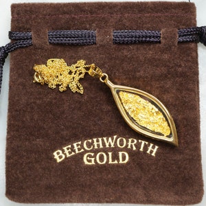 May include: A gold pendant necklace with a leaf-shaped charm containing real gold flakes. The pendant is displayed on a brown velvet pouch with the text "Beechworth Gold".