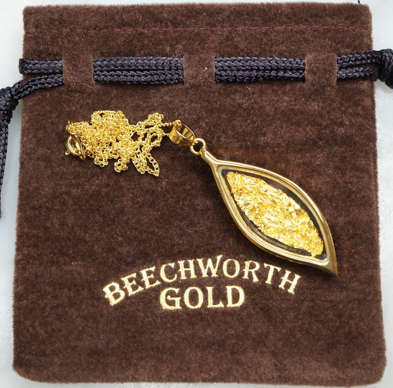 May include: A gold pendant necklace with a leaf-shaped charm containing real gold flakes. The pendant is displayed on a brown velvet pouch with the text "Beechworth Gold".