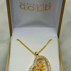 May include: A gold heart-shaped pendant necklace with a clear glass insert containing a piece of Australian gold. The necklace is in a white box with the words "Australian Gold" printed on the lid.