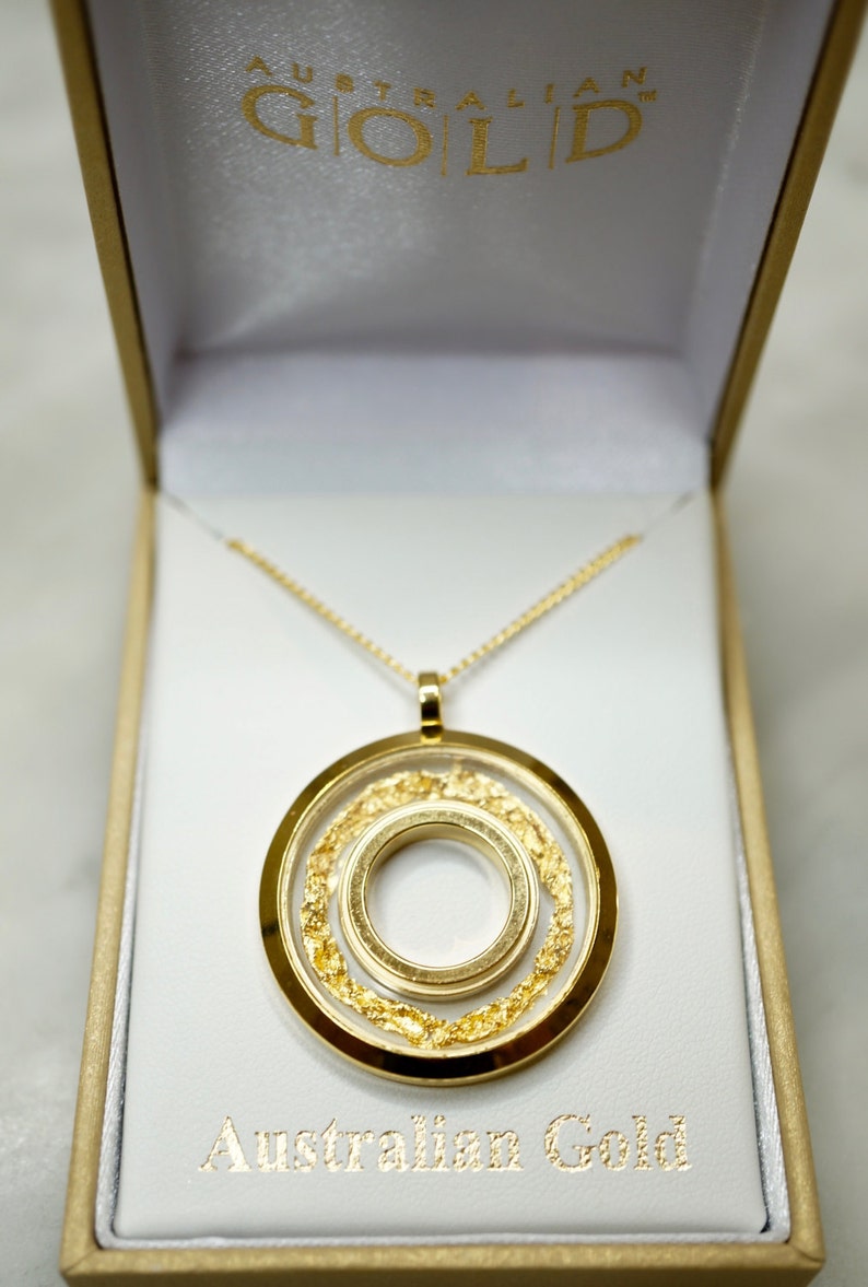 May include: A gold pendant necklace with a circular design, presented in a white box. The pendant features three concentric circles, with the middle circle filled with gold flakes. The box is labeled "Australian Gold".
