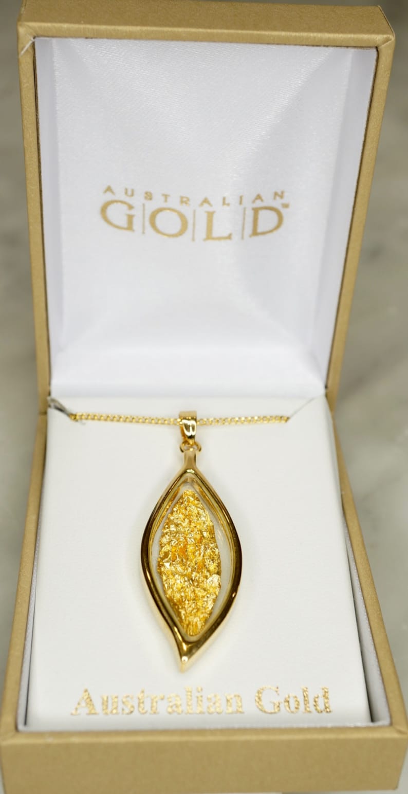 May include: A gold necklace with a pendant featuring a leaf-shaped design filled with real Australian gold flakes. The pendant is in a white box with the words "Australian Gold" printed on the box.