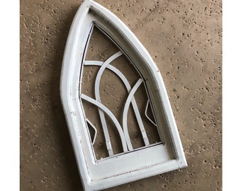 May include: White wooden arched window frame with a decorative, geometric, white metal design inside. The frame is distressed and has a rustic look.
