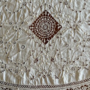 May include: White cotton tablecloth with intricate embroidered lace detailing. The centre features a large, openwork diamond design with a spiral motif. The border is a delicate crochet lace.