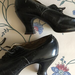 May include: A pair of black leather heeled shoes with lace-up fronts. The shoes have a vintage style and are in good condition.