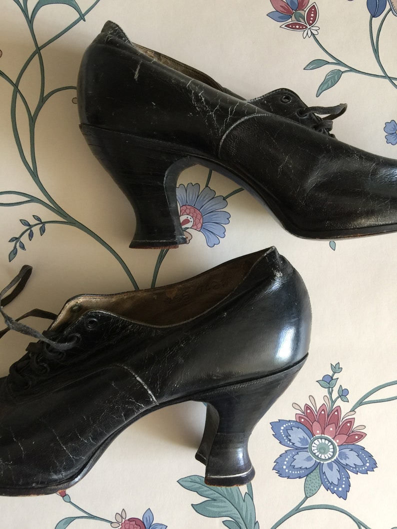May include: A pair of black leather heeled shoes with lace-up fronts. The shoes have a vintage style and are in good condition.