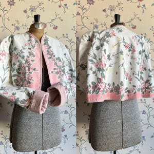 May include: A white and pink floral print cropped jacket with gingham trim. The jacket has a pink and green trim around the edges and a white gingham lining on the sleeves.