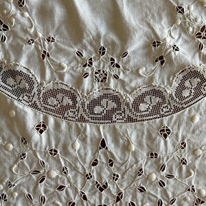 May include: White cotton tablecloth with delicate embroidered floral designs and a scalloped lace border.