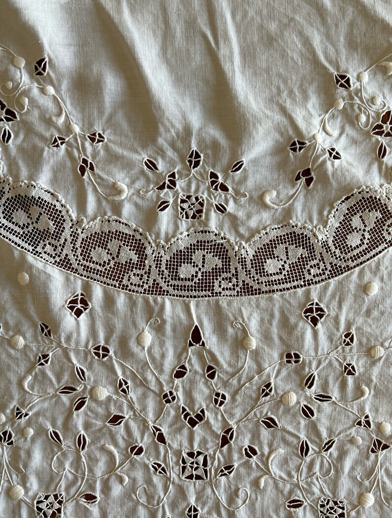 May include: White cotton tablecloth with delicate embroidered floral designs and a scalloped lace border.
