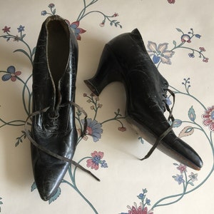 May include: A pair of black leather heeled shoes with lace-up fronts. The shoes have a pointed toe and a high heel.