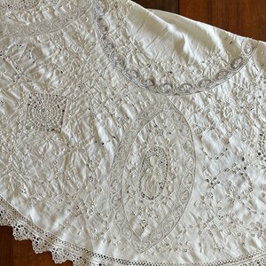 May include: A white round tablecloth with intricate lace embroidery and a scalloped edge.