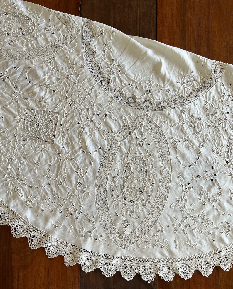 May include: A white round tablecloth with intricate lace embroidery and a scalloped edge.