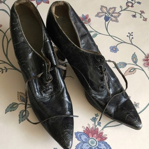 May include: A pair of black leather pointed-toe shoes with lace-up fronts. The shoes have a vintage look and are in good condition.