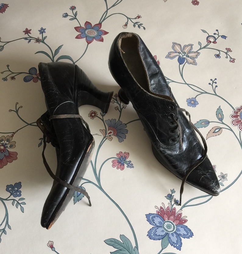 May include: A pair of black leather lace-up shoes with pointed toes and high heels. The shoes are worn and have a vintage look.