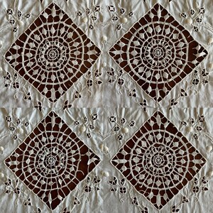 May include: White cotton fabric with a repeating pattern of intricate, cut-out lace designs. The lace features a circular motif with a central spiral and radiating lines.