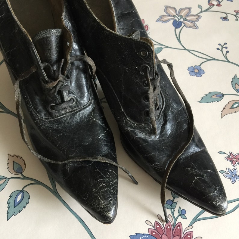 May include: A pair of black leather shoes with pointed toes and lace-up fronts. The shoes have a worn, vintage look.