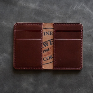 May include: A burgundy leather wallet with multiple card slots and a brown paper insert with the text "Genuine Leather,  J.W.  1905,  Co."