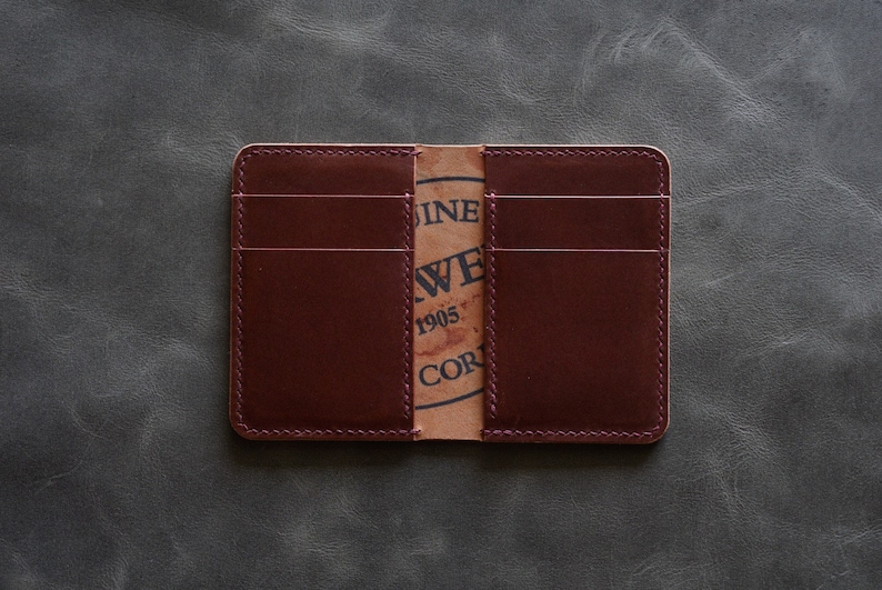 May include: A burgundy leather wallet with multiple card slots and a brown paper insert with the text "Genuine Leather,  J.W.  1905,  Co."