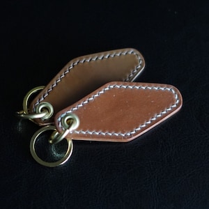 May include: Two brown leather keychains with stitched edges and gold metal key rings.