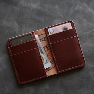 May include: A burgundy leather wallet with multiple card slots and a billfold. The wallet is open and shows a credit card, a driving licence, and a dollar bill.