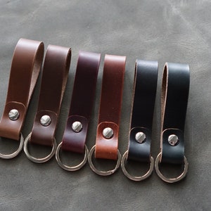 Pode incluir: Sete chaveiros de couro com argolas de prata. Os chaveiros são de diferentes cores: castanho, castanho escuro, bordô, castanho claro, preto e castanho escuro.