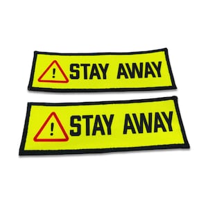 May include: Two rectangular patches with a bright yellow background and a black border. Each patch features a red-outlined yellow triangle containing a black exclamation point, followed by the bold black text STAY AWAY in capital letters.