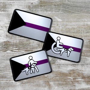 Op de afbeelding: Drie strijkbare patches met een zwarte driehoek en een paarse streep op een zilveren achtergrond. De patches tonen een persoon in een rolstoel met een hulphond, een persoon die een hulphond uitlaat en een persoon in een rolstoel met een hulphond.