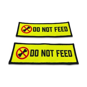 May include: Two rectangular embroidered patches with a bright yellow background and a black border. Each patch features the text DO NOT FEED in bold black capital letters next to a red circular prohibition symbol containing a black bone icon.