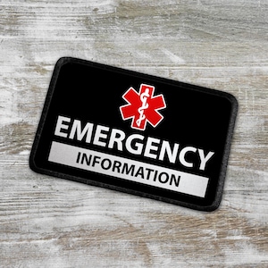 May include: Black patch with white text that reads "Emergency Information" and a red medical symbol with a snake and staff.
