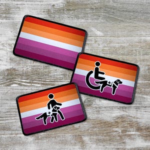 Könnte beinhalten: Rechteckige Aufnäher mit einem lesbischen Pride-Flaggen-Design und Symbolen für Assistenzhunde. Die Aufnäher weisen einen Farbverlauf aus orangefarbenen, roten, rosa und weißen Streifen auf. Einige Aufnäher zeigen eine Person im Rollstuhl mit einem Assistenzhund.