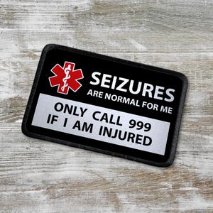 May include: Black rectangular patch with the text "SEIZURES ARE NORMAL FOR ME" and "ONLY CALL 999 IF I AM INJURED". The patch also features a red medical symbol.